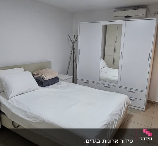 חדר שינה עם מיטה מסודרת וארון בגדים לבן